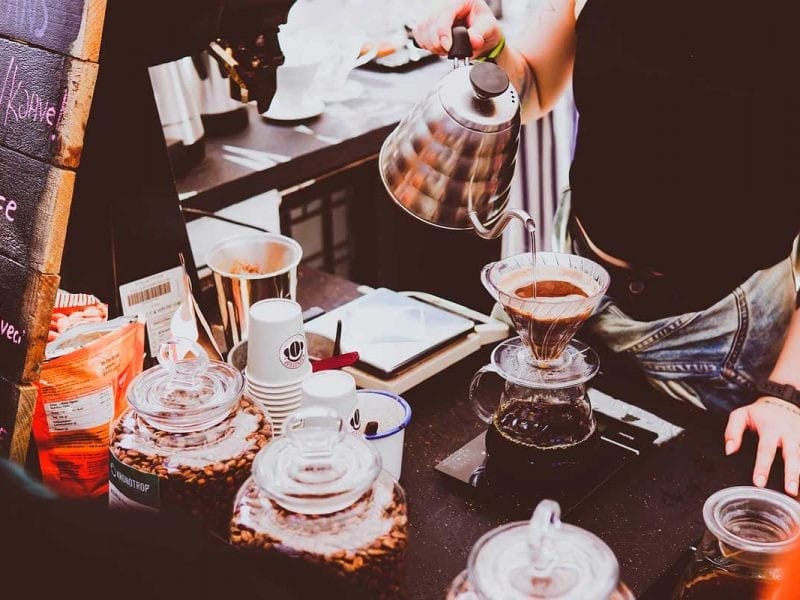 chica que sirve café con una cafetera y una taza especial en una mesa de una cafetería